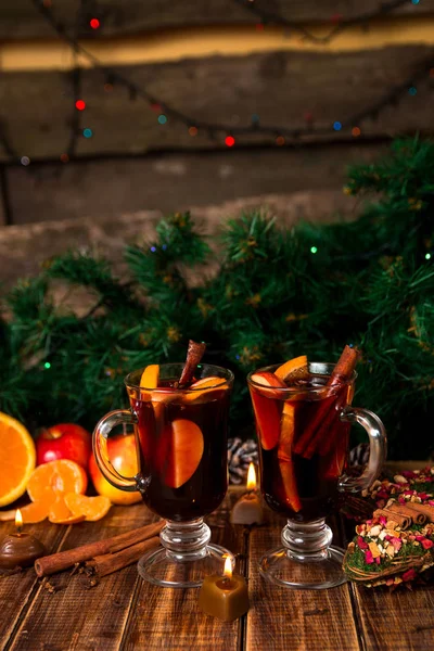 Ζεστό κρασί με φρούτα και μπαχαρικά σε ξύλινο τραπέζι. Διακοσμήσεις Χριστουγέννων στο υπόβαθρο. Χειμώνα του πλανήτη ποτό με συστατικά συνταγή γύρω. — Φωτογραφία Αρχείου