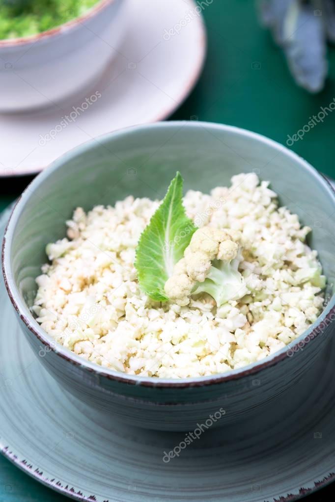 Cauliflower rice and broccoli rice in bowl on green background. Shredded.