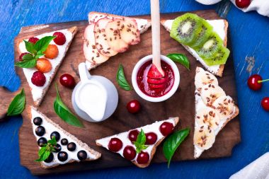 Ahşap rustik arka plan mavi tahtada meyve tost. Sağlıklı kahvaltı. Temiz yemek. Diyet kavramı. Tahıl ekmek dilimleri ile krem peynir ve çeşitli meyve, meyveler, tohumlar. Vejetaryen. Üstten Görünüm.