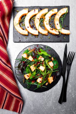 Sıcak kabak salatası karışık yaprak roka, pazı, içinde gri arka plan üzerinde siyah arduvaz plaka üzerinde. Izgara balkabağı. Üstten Görünüm