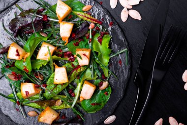 Sıcak kabak salatası karışık yaprak roka, pazı, içinde siyah arka plan üzerine siyah arduvaz plaka üzerinde. Izgara balkabağı. Üstten Görünüm