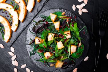 Sıcak kabak salatası karışık yaprak roka, pazı, içinde siyah arka plan üzerine siyah arduvaz plaka üzerinde. Izgara balkabağı. Üstten Görünüm