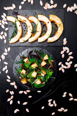 Sıcak kabak salatası karışık yaprak roka, pazı, içinde siyah arka plan üzerine siyah arduvaz plaka üzerinde. Izgara balkabağı. Üstten Görünüm