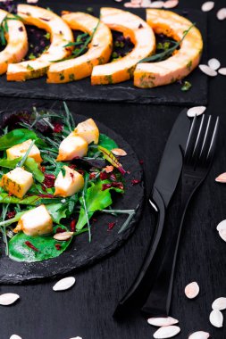 Sıcak kabak salatası karışık yaprak roka, pazı, içinde siyah arka plan üzerine siyah arduvaz plaka üzerinde. Izgara balkabağı. Yakın çekim.