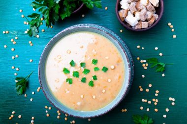 Yeşil ahşap zemin üzerine yeşil kase bezelye çorbası. Üstten Görünüm. Kuru sarı bezelye. Vegan gıda.