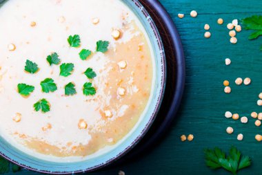 Yeşil ahşap zemin üzerine yeşil kase bezelye çorbası. Üstten Görünüm. Kuru sarı bezelye. Vegan gıda.