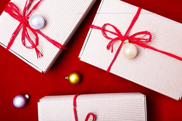 Karácsonyi díszdobozban. Karácsonyi ajándékokat a kézműves dobozok és piros szalag, piros háttér. Lapos másol hely feküdt. Lapos laikus stílus. Szemközti nézet. — Stock Fotó