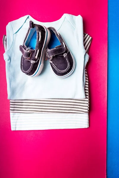 Carrocería plegada azul con zapatos de barco sobre fondo minimalista rosa y azul. pañal para recién nacido. Montón de ropa infantil. Traje de niño. Vista superior —  Fotos de Stock