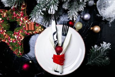 Noel tablo yer ayarını. Tatil arka plan. Beyaz tabak, bıçak ve çatal ile Noel süslemeleri siyah masada. Üstten Görünüm.