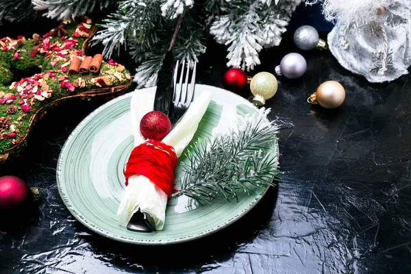 Christmas table place setting. Holidays background. Green plate, knife and fork with christmas decorations on black table. Top view. — Stock Photo, Image