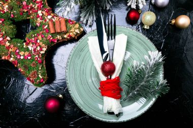 Noel tablo yer ayarını. Tatil arka plan. Yeşil plaka, bıçak ve çatal ile Noel süslemeleri siyah masada. Üstten Görünüm.