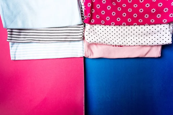 布料缝制。折叠蓝色和粉红色衣在简约粉红色和蓝色背景。尿布为新生男孩和女孩。一堆婴儿服装。儿童服装。顶部视图 — 图库照片