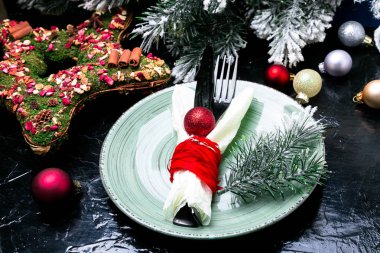 Noel tablo yer ayarını. Tatil arka plan. Yeşil plaka, bıçak ve çatal ile Noel süslemeleri siyah masada. Üstten Görünüm.