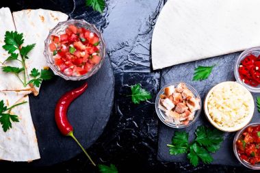 Mexican quesadilla ve siyah arduvaz taş plaka üzerinde salsa malzemelerle. Üstten Görünüm