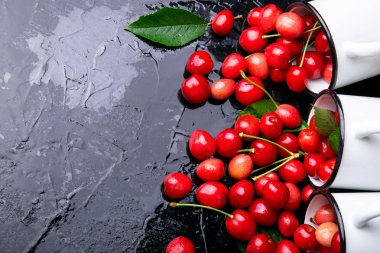 Dağınık kiraz emaye bardak dan. Kiraz demir Kupası siyah arka plan üzerine. Sağlıklı, yaz meyve. Kiraz. Üç. Üstten Görünüm.