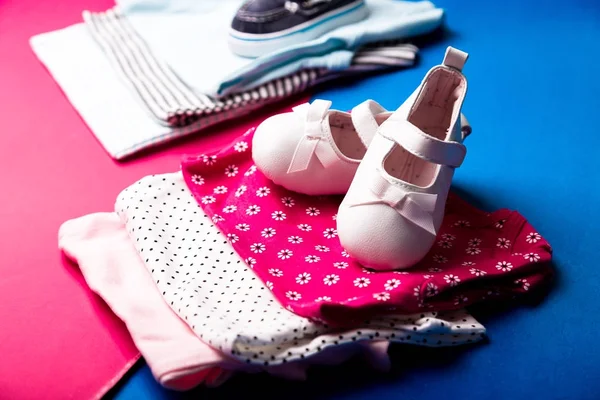 Body plié bleu et rose avec des chaussures de bateau sur un fond rose et bleu minimaliste. couche pour nouveau-né garçon et fille. Une pile de vêtements pour bébés. Tenue enfant — Photo