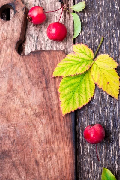 Hojas y pequeña manzana alrededor de la tabla de cortar vacía sobre fondo rústico de madera. Vista superior. Una trampa. Copiar espacio. Día de Acción de Gracias. Puesta plana . —  Fotos de Stock