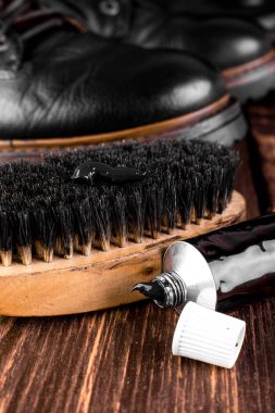 Parlatma donanımları, fırça ve Lehçe krem ile ahşap arka plan üzerinde siyah çizmeler. Makro. Portre.