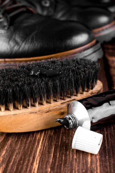 Parlatma donanımları, fırça ve Lehçe krem ile ahşap arka plan üzerinde siyah çizmeler. Makro. Portre.