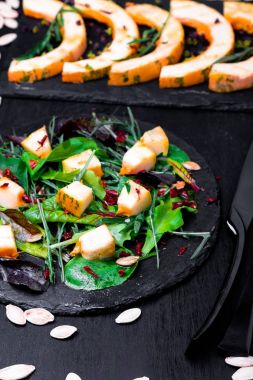 Sıcak kabak salatası karışık yaprak roka, pazı, içinde siyah arka plan üzerine siyah arduvaz plaka üzerinde. Izgara balkabağı. Üstten Görünüm