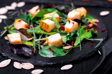 Sıcak kabak salatası karışık yaprak roka, pazı, içinde siyah arka plan üzerine siyah arduvaz plaka üzerinde. Izgara balkabağı. Yakın çekim.