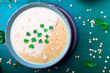 Yeşil ahşap zemin üzerine yeşil kase bezelye çorbası. Üstten Görünüm. Kuru sarı bezelye. Vegan gıda.