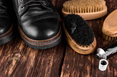 Parlatma donanımları, fırça ve Lehçe krem ile ahşap arka plan üzerinde siyah çizmeler. 