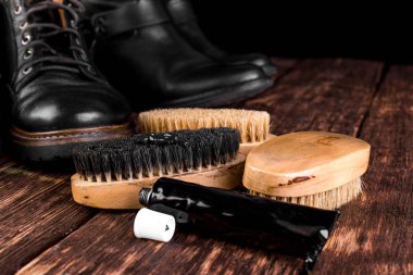 Parlatma donanımları, fırça ve Lehçe krem ile ahşap arka plan üzerinde siyah çizmeler. 