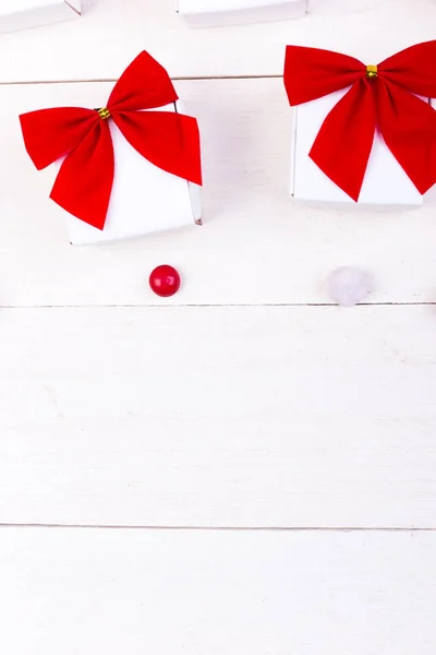 Prezenty świąteczne, biały pudełeczka z czerwoną kokardką i cukierki na białym tle drewnianych. Leżał z płaskim. Wesołych Świąt Bożego Narodzenia. — Zdjęcie stockowe