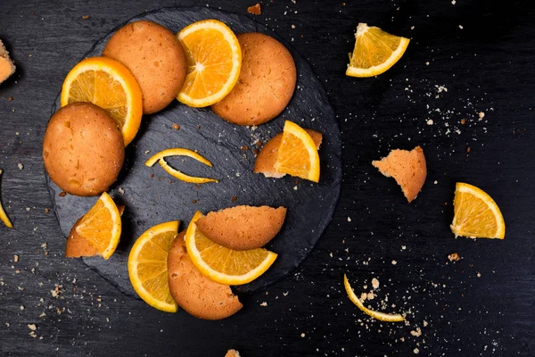Cookies en oranje citrusvruchten op leisteen plaat op zwarte achtergrond. Plat leggen — Stockfoto