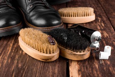 Parlatma donanımları, fırça ve Lehçe krem ile ahşap arka plan üzerinde siyah çizmeler. 