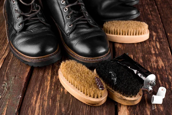 Black boots on wooden background with polishing equipment, brush and polish cream. — Stock Photo, Image