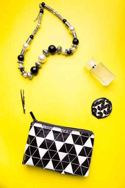 Woman handbag with makeup and accessories on yellow background. Flat lay