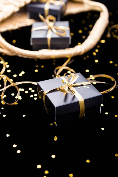 Cajas de regalo negras con cinta de oro salen de la bolsa de oro sobre fondo brillante. De cerca. . — Foto de Stock