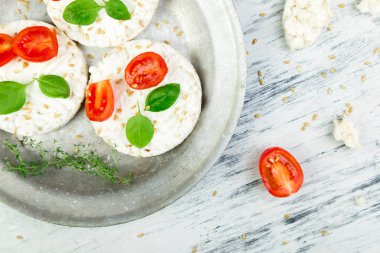 Sağlıklı pirinç kek kiraz domates, peynir beyaz peynir, fesleğen ve susam beyaz zemin üzerine metal plaka. Diyet çerez. Üstten Görünüm.