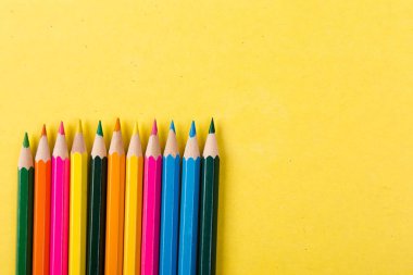 Sarı arka plan üzerinde renkli kalemler. Düz yatıyordu. Kopya alanı.