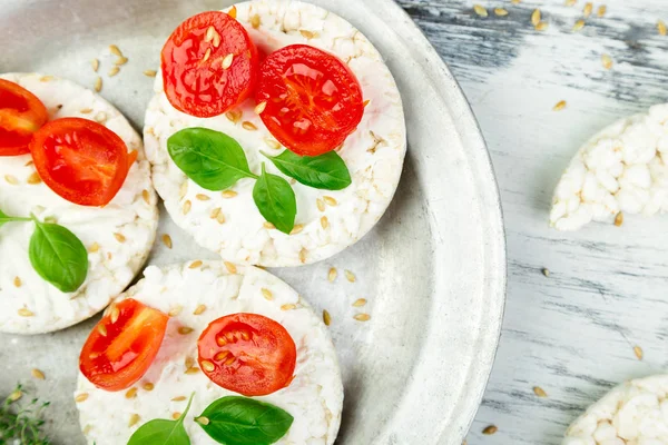 Healthy Rice Cakes with cherry tomatoes, cheese feta, basil and sesame in metal plate on white background. Diet snack.  Top view.