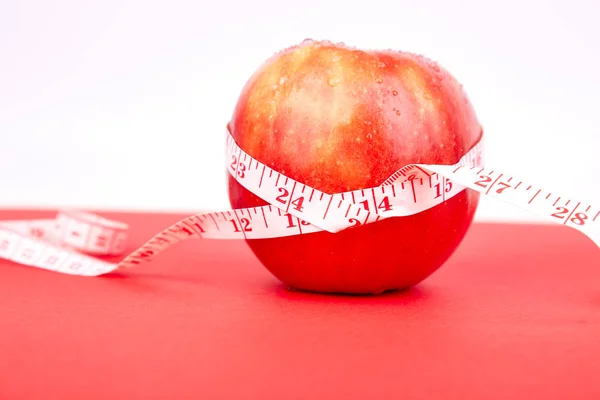 Measuring tape wrapped around a red apple as a symbol of diet on red paper background. Weight loss concept. Diet. Dieting concept. Vegan. Clear food. Healthy. Minimalism