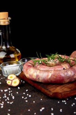 Biberiye, tuz ve peper ahşap kesme tahtası üzerinde ham sarmal domuz sosisi.