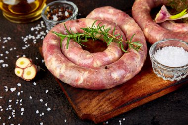 Biberiye, tuz ve peper ahşap kesme tahtası üzerinde ham sarmal domuz sosisi.