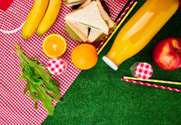 Picnic on the grass. Red checked tablecloth, basket, healthy food sandwich and fruit, orange juice. Top view.  Summer Time Rest. Flat lay.