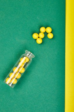 Tıbbi blog için minimalizm tarzı şablon. Küçük cam şişe küçük sarı ve yeşil haplar kağıt arka plandan döküldü. Eczacılık konsepti. İlaç hapları. Düz la