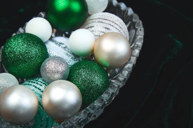 Noel ya da yeni yıl hazırlıkları. Yeşil, beyaz ve gümüş Noel ağacı süsleme oyuncakları, toplar, koyu arka plandaki cam kutuda, üst manzara. Bayram havası.