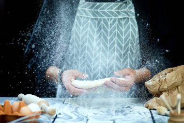 Adam, aşçı hamuru fırlatıyor, uçuyor, donuyor. Siyah bir arka planda. Havaya uçan beyaz un. Eller hamuru hazırlıyor