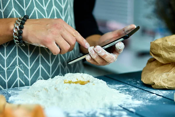 Man using electronic tablet pc in kitchen for baking. Man searching for food recipe in tablet computer. Close up man touching tablet screen and browsing recipes.