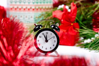 Siyah Alarm saati ve köknar ağacı dalı, beyaz ahşap arka planda kırmızı Noel süslemeleri. Eve Time Concept masada. Yeni yıl yaklaşıyor. Noel hediyesi kartı..