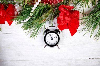Siyah Alarm saati ve köknar ağacı dalı, beyaz ahşap arka planda kırmızı Noel süslemeleri. Eve Time Concept masada. Yeni yıl yaklaşıyor. Düz yerde, üst tarafta. Noel hediyesi kartı..