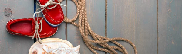 Banner of Red boat shoes near big shell and rope on wooden background.