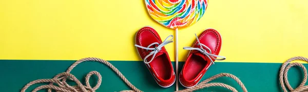 Banner of Small red boat shoes near big multi-colored lollipop and rope on colored background.