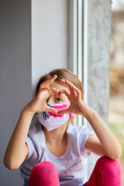Küçük kız, maskeli çocuk ellerinden kalp yapıyor, koronavirüs karantinası